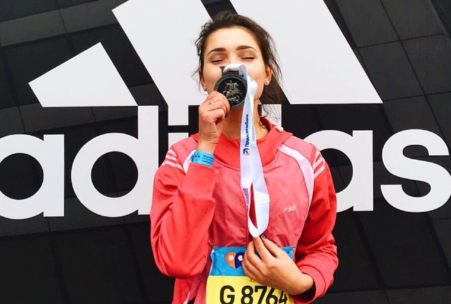 Девушка целует медаль финишера марафона на фоне логотипа adidas