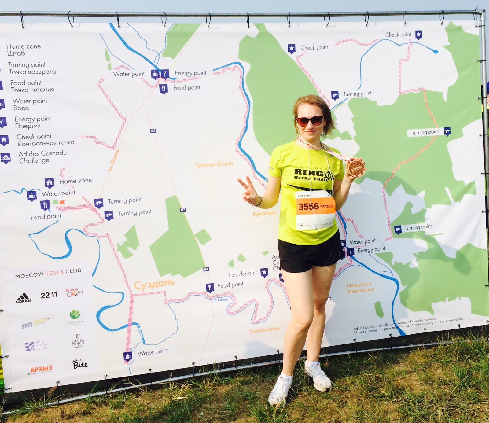 Женщина с медалью финишера Ring 100 Ultra Trail позирует у карты трассы забега