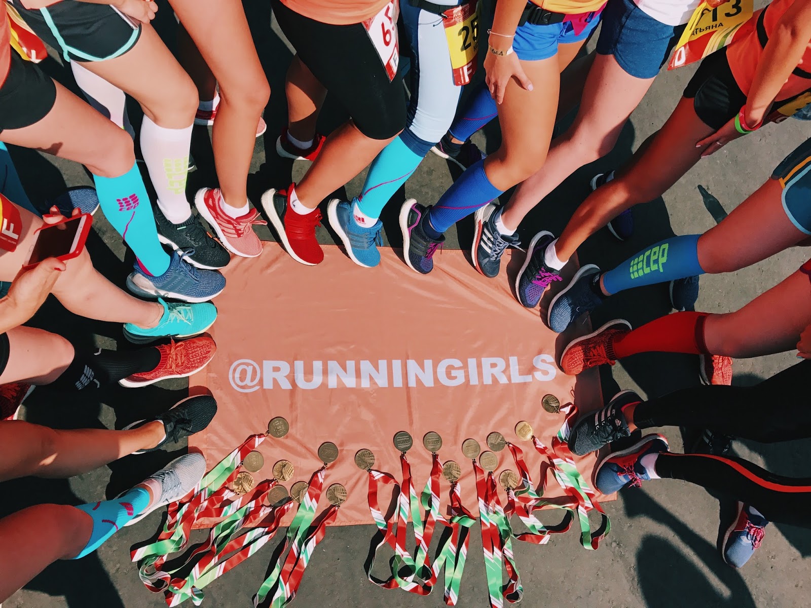 Ноги бегунов в круге вокруг баннера RUNNINGIRLS с медалями