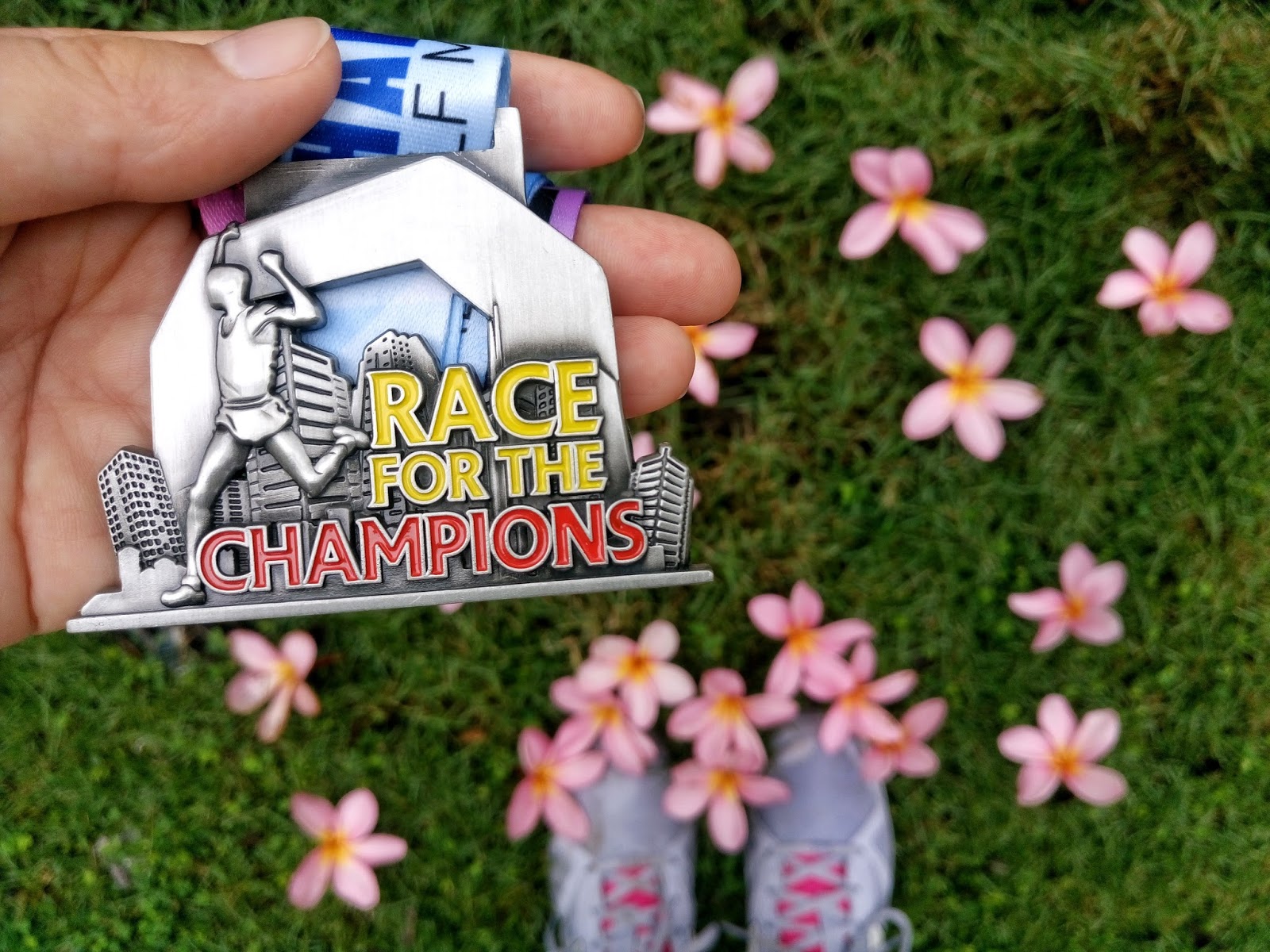 Медаль забега Race for the Champions в руке на фоне травы и цветов